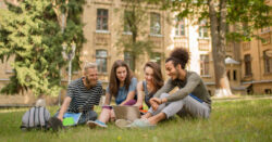View of smiling college students sitting on grass on sunny day..