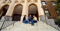 Image of three students sitting and talking on the steps of a college building.