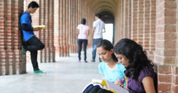 Image of five college students in an outdoor colonnade, talking and studying.