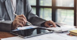 Close-up image of a nonprofit leader working on a tablet at a desk covered with documents showing various graphs